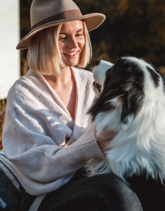 Person wearing a hat smiles at a fluffy black and white dog.