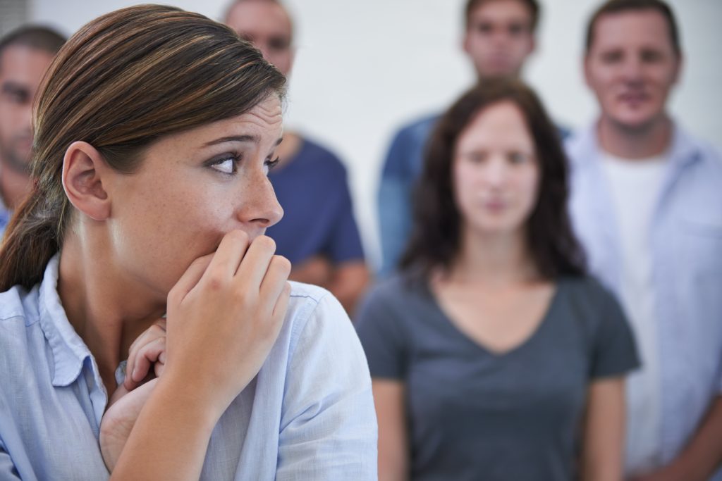 A woman in the foreground looks anxious, with her hand near her face—an embodiment of understanding anxiety. Meanwhile, a group of people stands in the blurred background, highlighting the importance of mental health awareness.